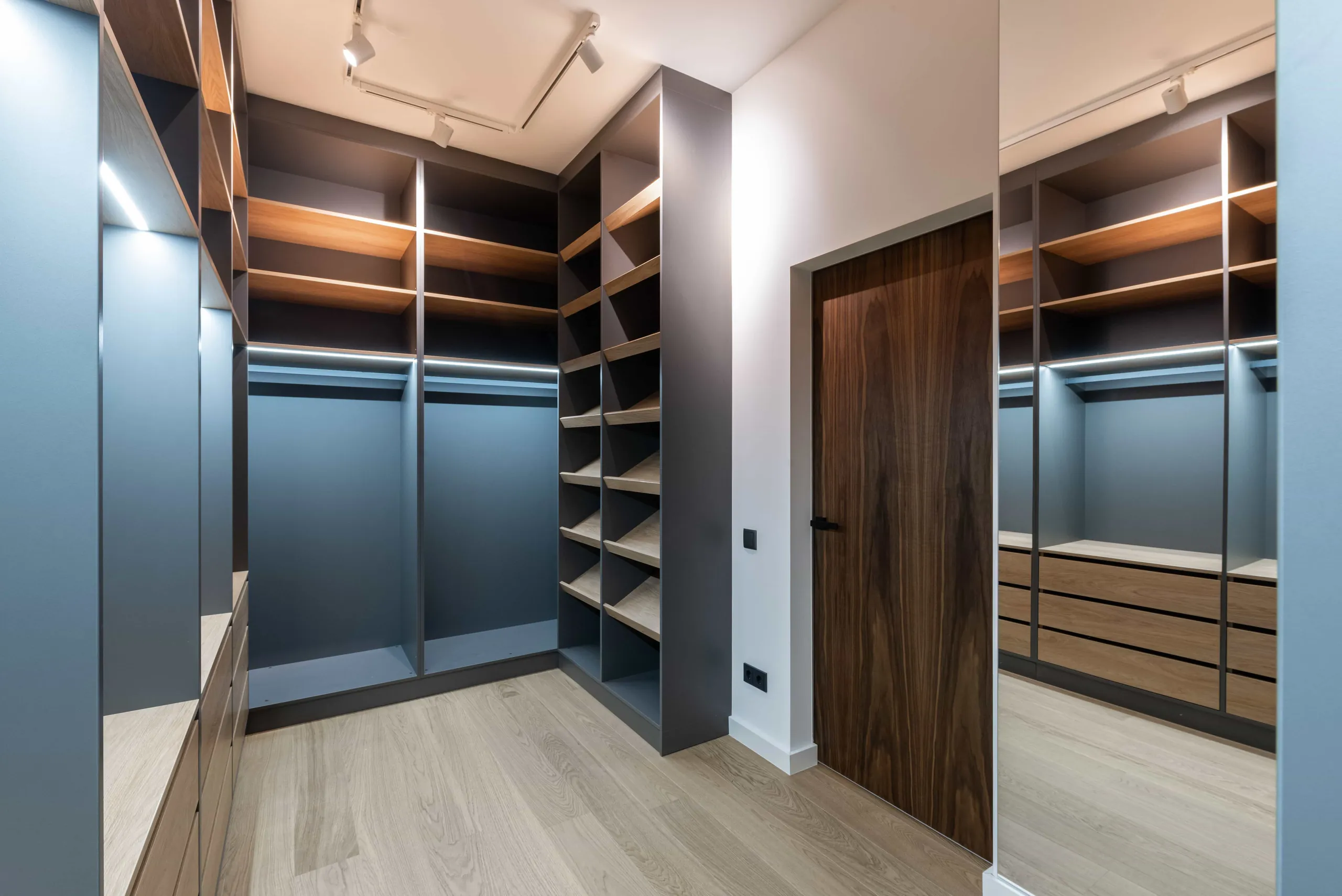 Walk-in closet with grey-blue cabinets, lit walnut shelves, drawers and long hanging space
