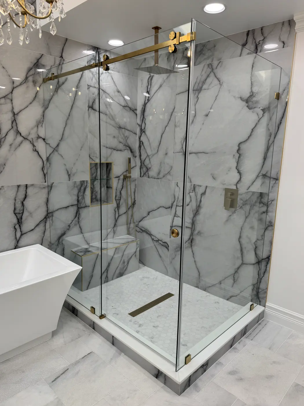 Corner shower in white and grey veined marble with brass hardware and a brass header bar