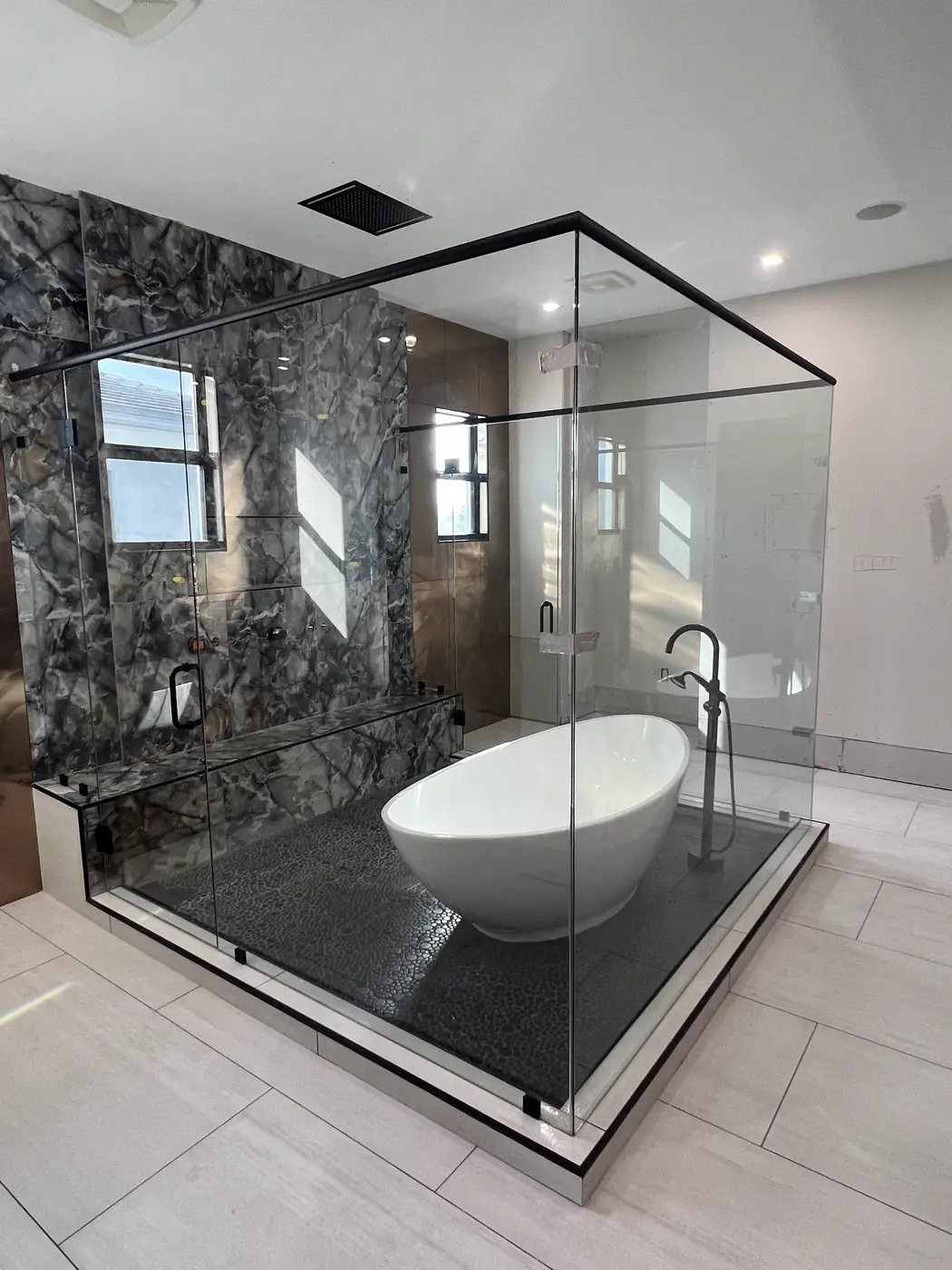Glass enclosure around a freestanding tub on a black stone floor, with a black top frame