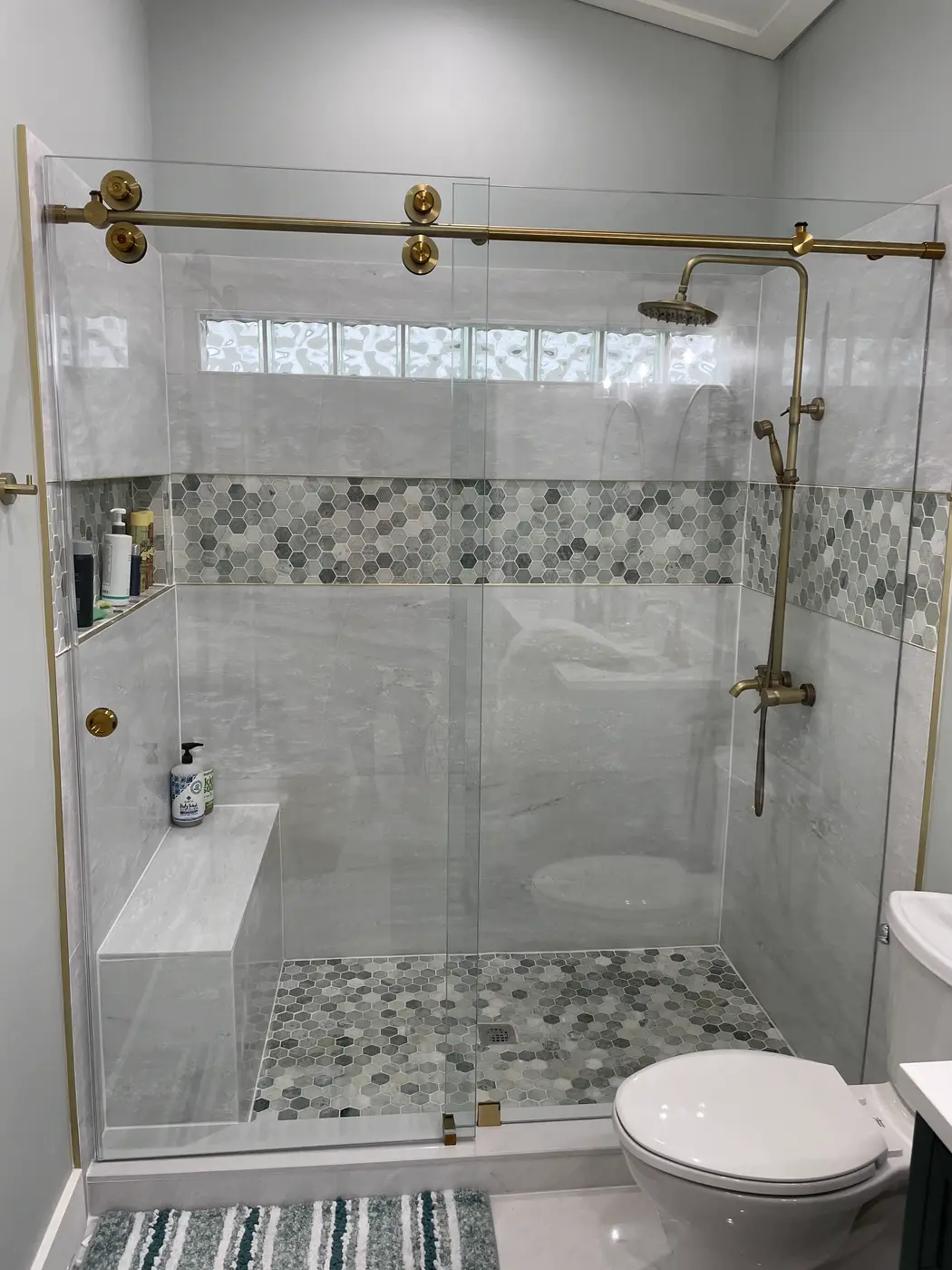 Sliding glass shower door on a brass roller bar over a mosaic tile floor