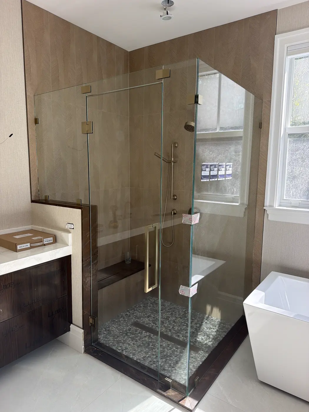 Corner shower against a wood-look tile wall with brushed brass hinges and handle