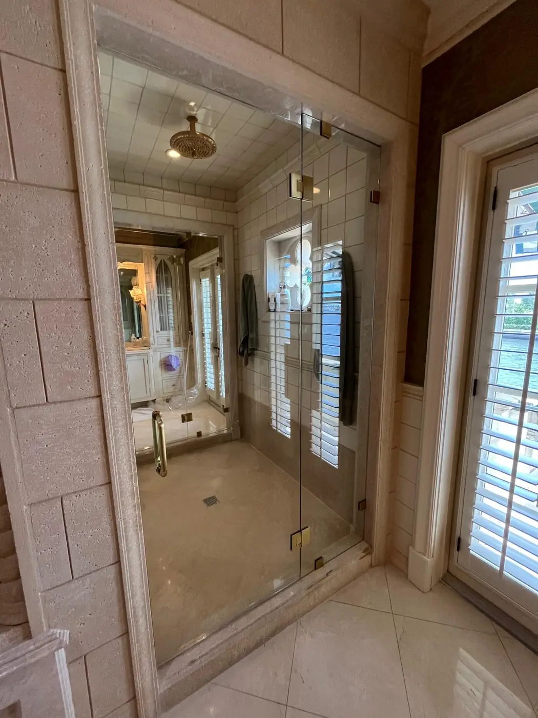 Full-height glass shower door between stone walls with a rain shower head