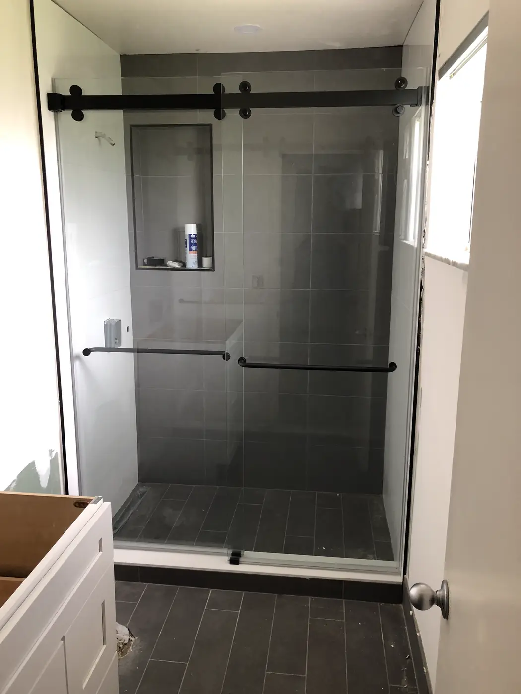 Sliding shower door with a matte black roller bar and towel bar