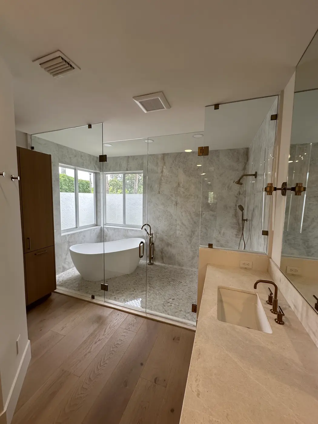 Glass shower enclosure beside a freestanding tub in a bathroom with wood floors