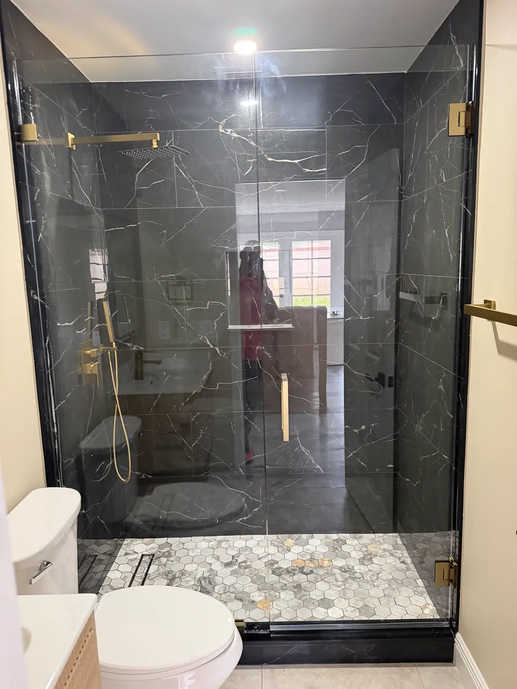 Shower with dark marble walls and brushed brass hinges and handle