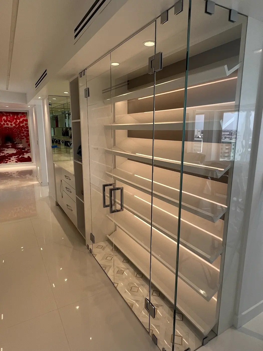 Frameless glass doors in front of lit shelving