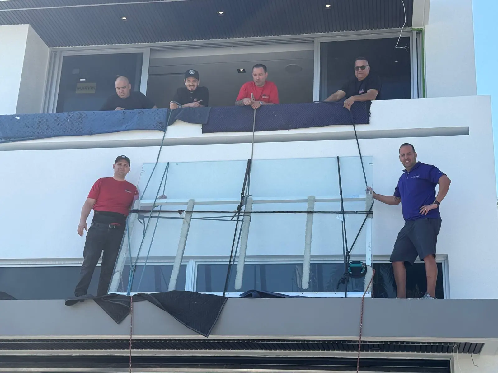 Galaxy Glass crew members setting glass railing panels on a second-floor balcony