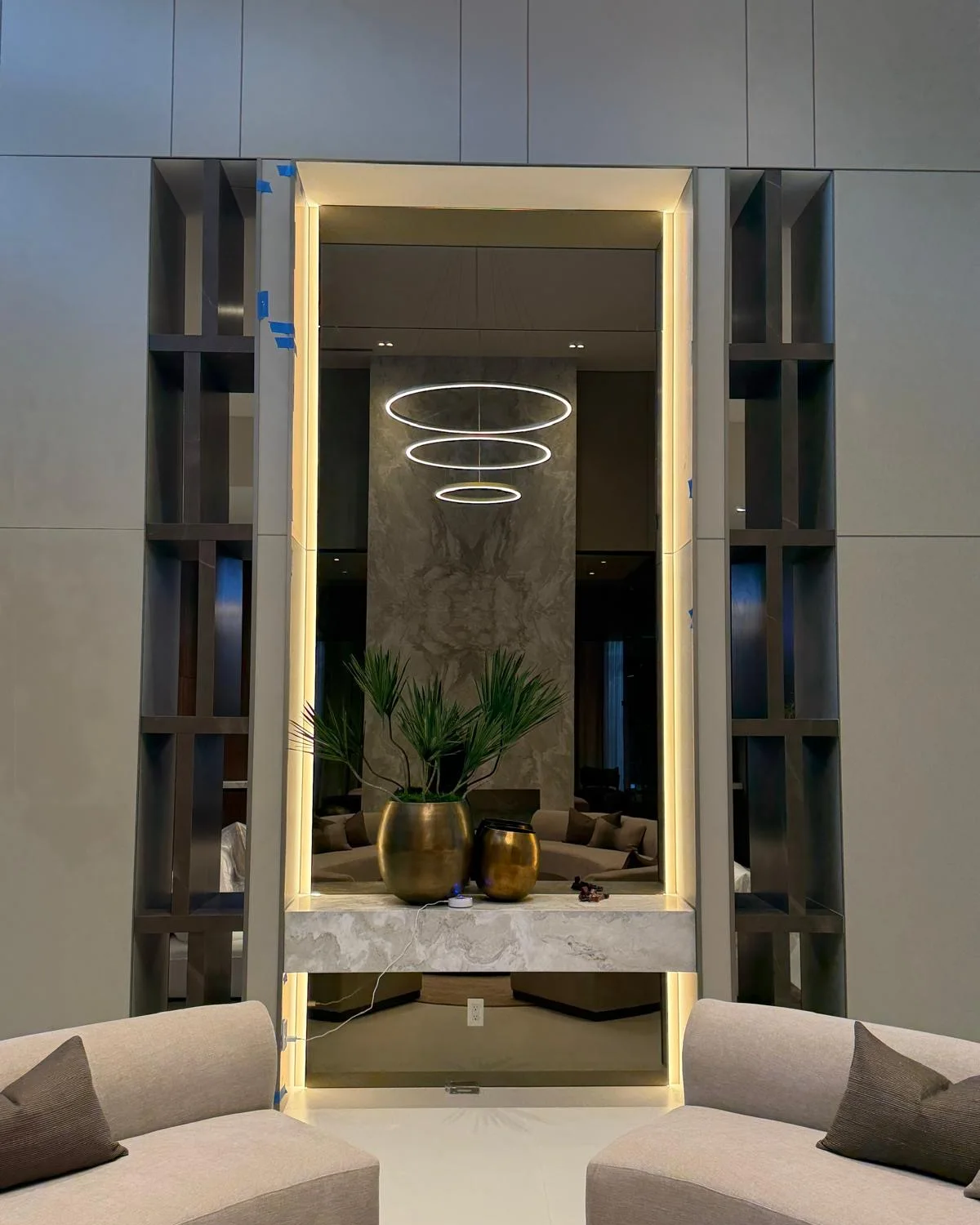 Floor-to-ceiling mirror with LED lighting around the frame, set between dark shelving above a stone console