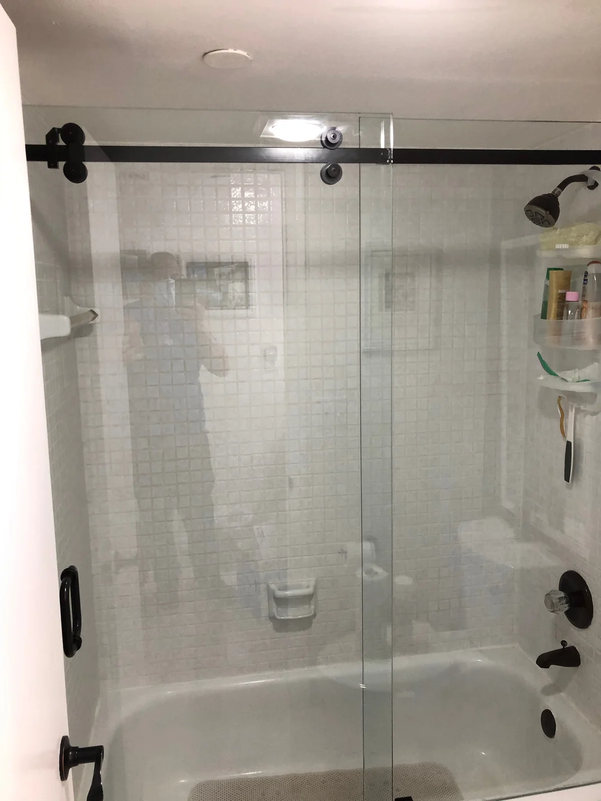 Sliding glass shower door on exposed black rollers over a tub