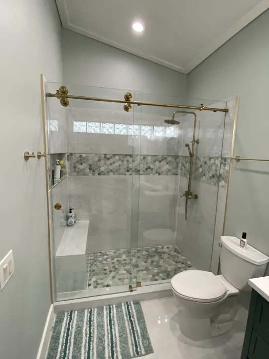 Sliding shower door on brass rollers with a mosaic tile band