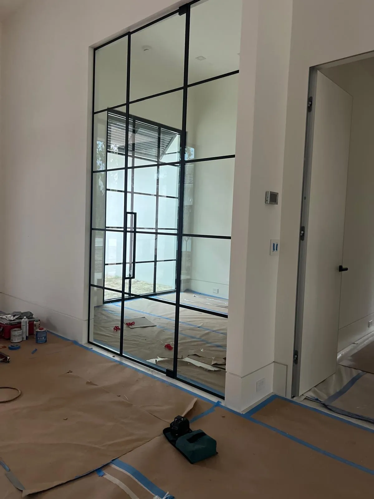 Black grid glass partition installed on a job site with the floor still covered